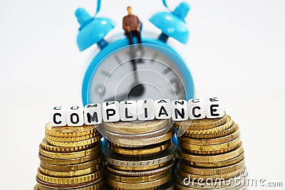 Businessman plastic figurine sitting on alarm clock, busy with compliance procedures â€“ compliance word on stack on cash money Stock Photo